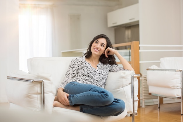 Jeune femme rêvant assise sur un canapé à la maison