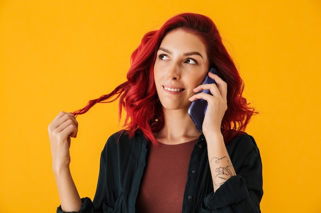 Jeune femme rêvante aux cheveux roux bouclés parlant au téléphone portable isolé