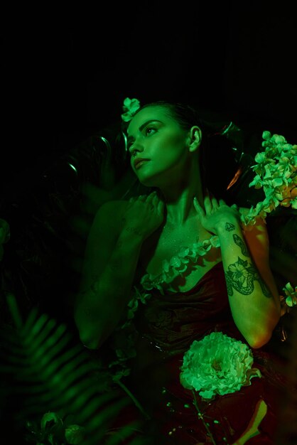 une jeune femme rêveur de couleur verte avec les cheveux mouillés détournant le regard et posant parmi les fleurs d'élégance