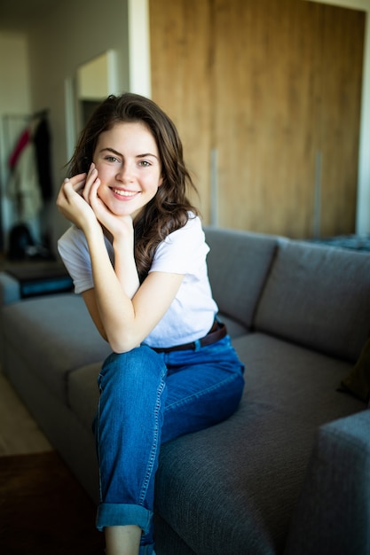 Jeune femme rêveuse assise sur un canapé à la maison.