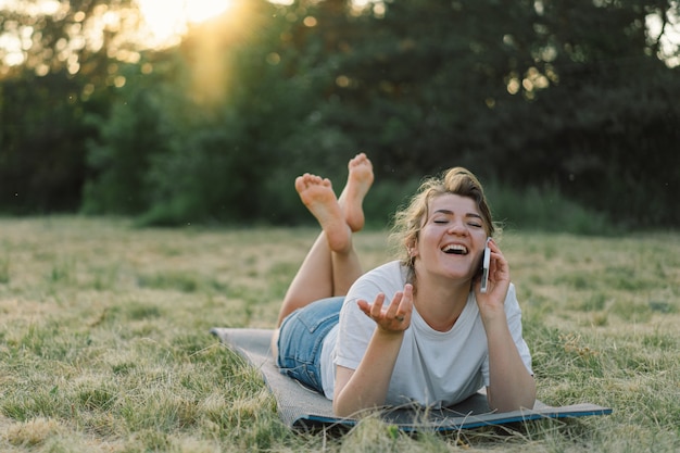 Jeune femme rit et parle au téléphone dans le pré au coucher du soleil femme utilisant un téléphone portable le con...