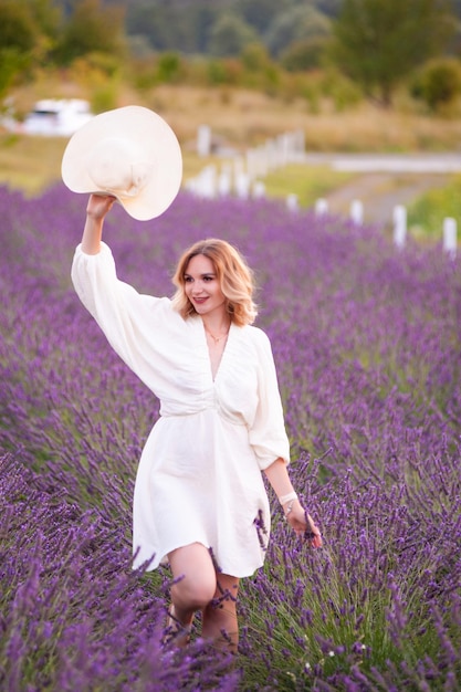 Jeune femme en robe blanche et chapeau de paille courant dans un champ de lavande