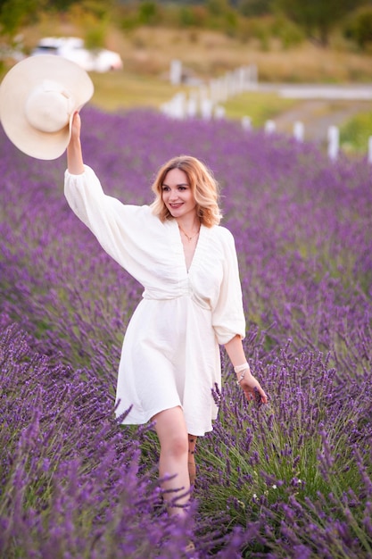 Jeune femme en robe blanche et chapeau de paille courant dans un champ de lavande