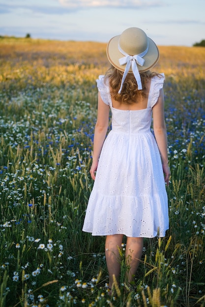 Photo jeune femme en robe blanche et chapeau vintage dans un pré avec de belles fleurs sauvages