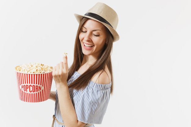 Jeune femme en robe bleue, chapeau regardant un film de cinéma tenant manger du pop-corn du seau isolé sur fond blanc. Gens, émotions sincères au cinéma, concept de style de vie. Espace publicitaire. Espace de copie.