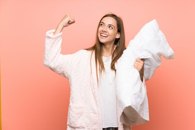 Jeune femme en robe de chambre sur un mur rose célébrant une victoire