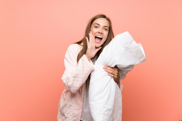 Jeune femme en robe de chambre sur un mur rose criant avec la bouche grande ouverte