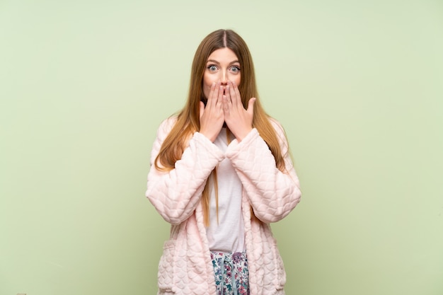 Jeune femme en robe de chambre sur un mur vert avec une expression faciale surprise