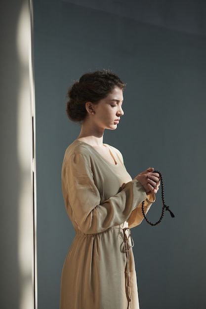 Jeune femme en robe et avec chapelet debout et priant les yeux fermés