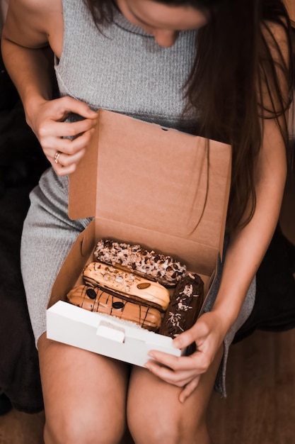 Jeune femme en robe courte tient sur ses genoux une boîte blanche ouverte avec des éclairs dessert français traditionnel