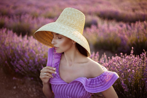 Une jeune femme en robe courte violette et chapeau de paille se tient dans un champ avec de la lavande en Crimée au coucher du soleil