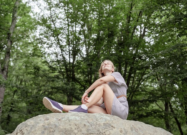 Jeune femme en robe d'été assise sur une grosse pierre dans la forêt à l'écart