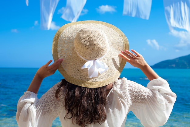 Jeune femme en robe d'été avec chapeau de paille à la recherche d'un ciel et d'une mer