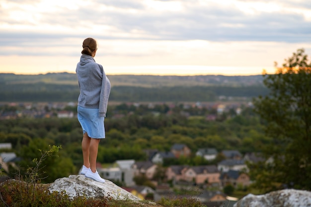 Une jeune femme en robe d'été debout à l'extérieur en profitant de la vue sur le coucher du soleil jaune vif.