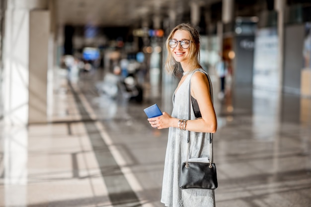 Jeune femme en robe grise debout avec des cartes d'embarquement dans le hall de départ de l'aéroport en attente du vol