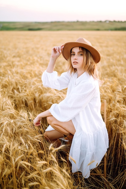 Jeune femme en robe de lin blanc et chapeau profitant d'une journée ensoleillée dans un champ de blé doré
