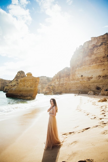 jeune femme en robe longue marchant sur la plage près de l'océan.