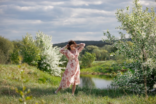 Jeune femme en robe longue se promène dans le jardin de printemps près du lac. La fille se repose dans la nature, le printemps est arrivé