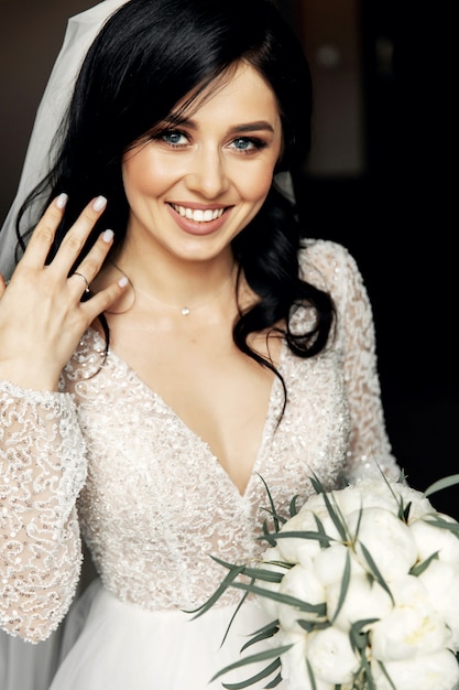 Jeune femme en robe de mariée, boire du vin sur le lit dans un intérieur luxueux.