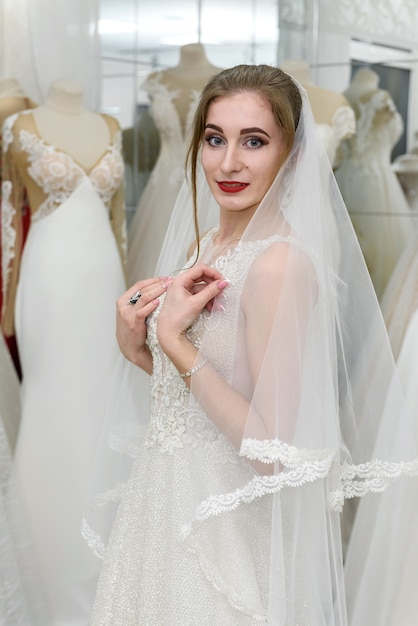 Jeune femme en robe de mariée et voile en boutique de mariée