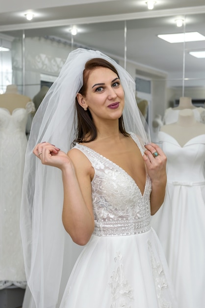 Jeune femme en robe de mariée et voile en boutique de mariée