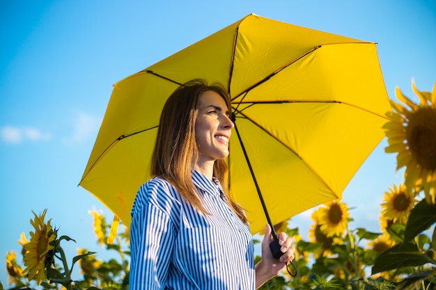 Jeune femme en robe et parapluie jaune sur un champ de tournesols.