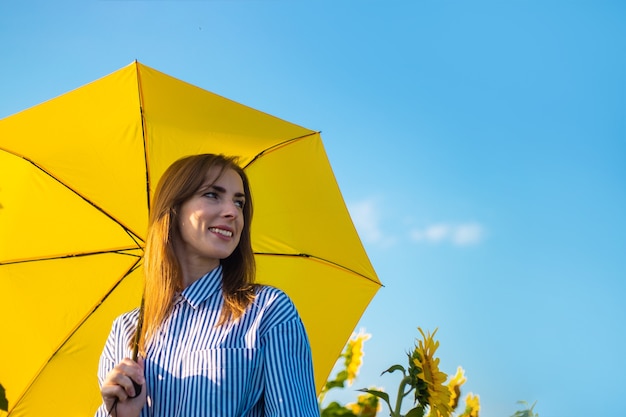 Jeune femme en robe et parapluie jaune sur un champ de tournesols.