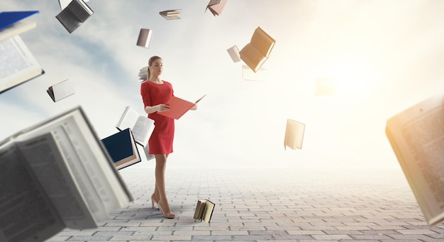 Jeune femme en robe rouge lisant un livre avec d'autres livres volant autour. Technique mixte