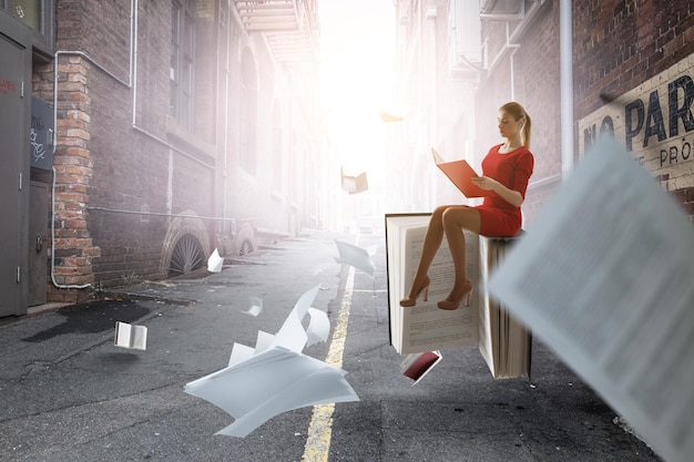 Jeune femme en robe rouge lisant un livre avec d'autres livres volant autour. Technique mixte