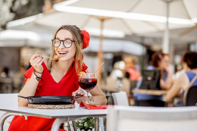 Jeune femme en robe rouge mangeant de la mer Paella, plat de riz traditionnel valencien, assis à l'extérieur au restaurant à Valence, Espagne