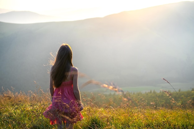 Jeune femme en robe rouge marchant sur un terrain en herbe lors d'une soirée venteuse dans les montagnes d'automne