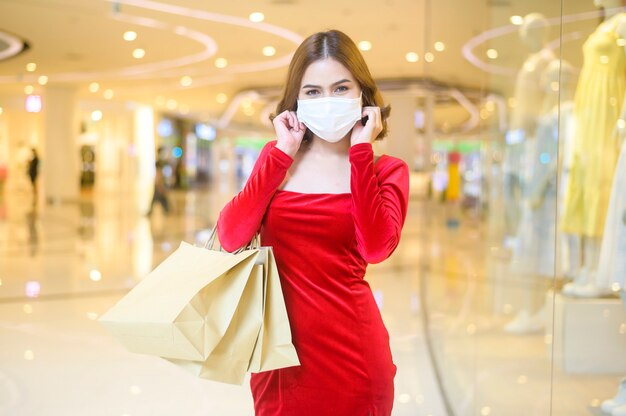 Une jeune femme en robe rouge portant un masque de protection dans un centre commercial