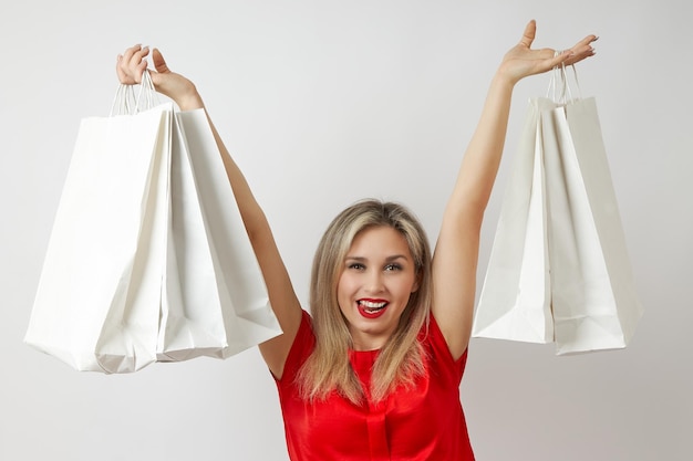 Jeune femme en robe rouge avec des sacs à provisions dans ses mains sur un fond blanc