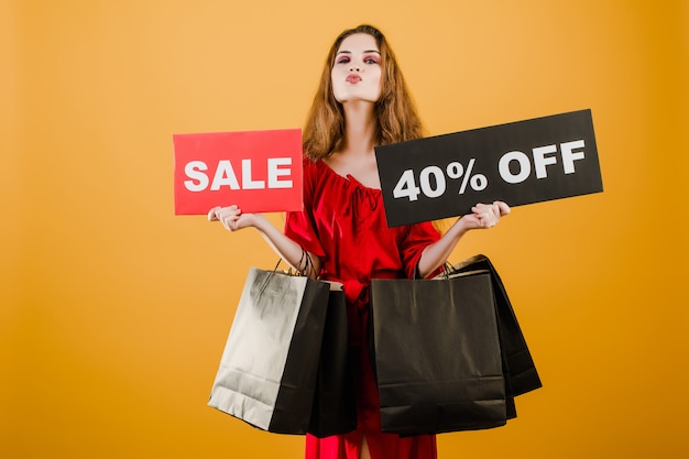 Jeune femme en robe rouge avec signe de vente 40% et sacs papier isolés sur jaune