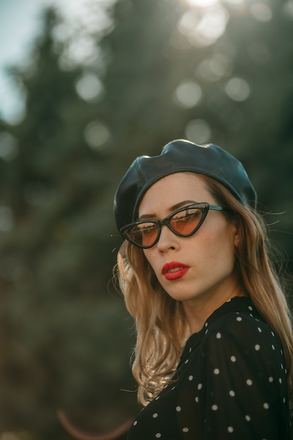 Jeune femme en robe vintage noire à pois posant à l'extérieur