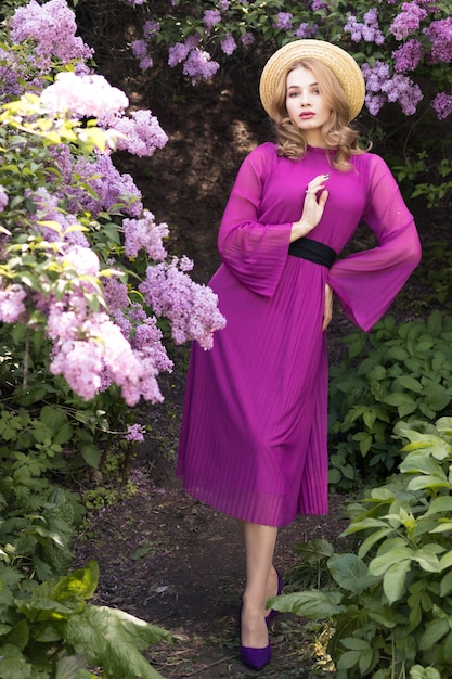 jeune femme en robe violette posant dans un jardin de lilas en fleurs