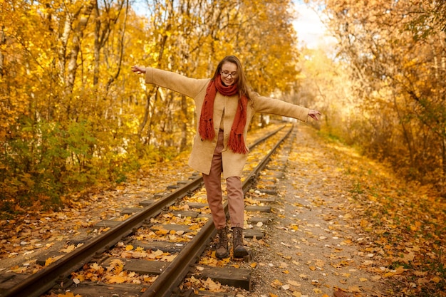 Jeune femme romantique en équilibre sur le chemin de fer recouvert de feuilles d'or sur fond d'automne