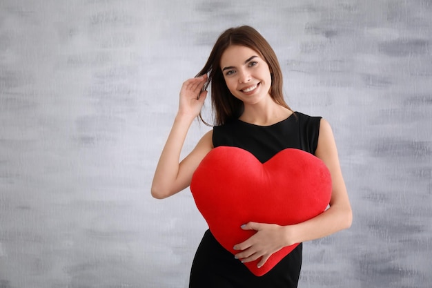 Jeune femme romantique avec oreiller en forme de coeur sur fond clair