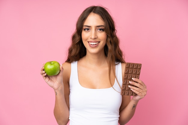 Jeune femme rose prenant une tablette de chocolat dans une main et une pomme dans l'autre