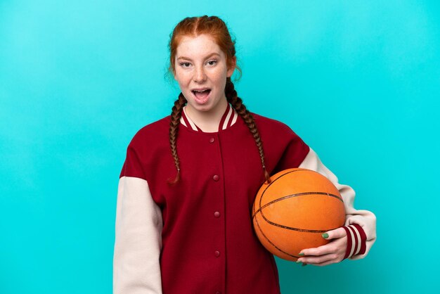 Jeune femme rougeâtre jouant au basketball isolée sur fond bleu avec une expression faciale surprise