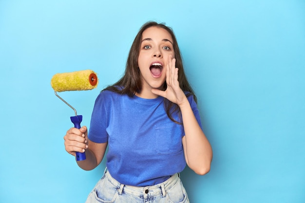 Une jeune femme avec un rouleau de peinture jaune sur un fond bleu criant et tenant la paume