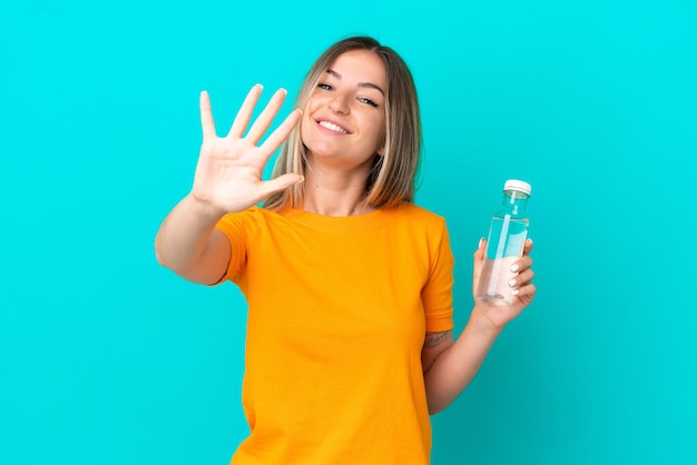 Jeune femme roumaine avec une bouteille d'eau isolée sur fond bleu comptant cinq avec les doigts