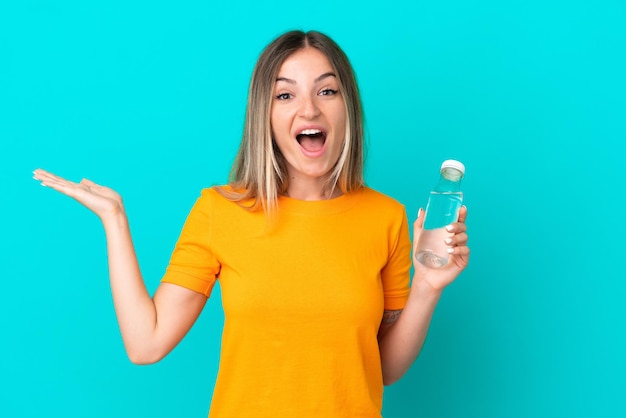 Jeune femme roumaine avec une bouteille d'eau isolée sur fond bleu avec une expression faciale choquée