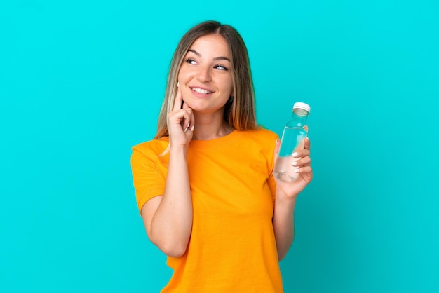 Jeune femme roumaine avec une bouteille d'eau isolée sur fond bleu pensant à une idée tout en levant les yeux