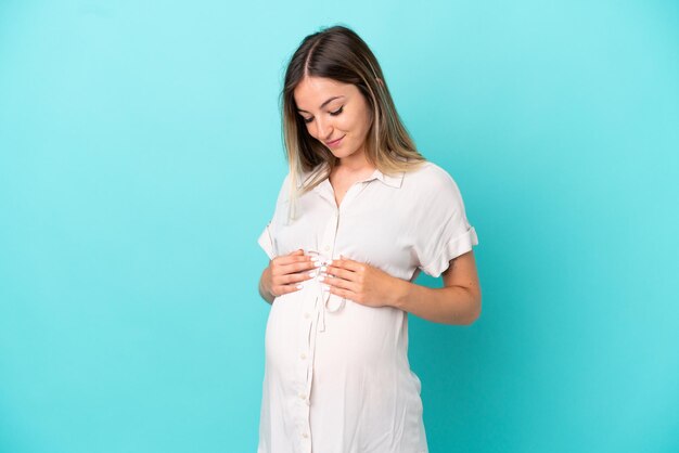 Jeune femme roumaine isolée sur fond bleu enceinte et heureuse