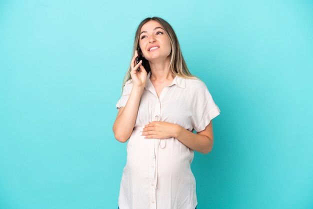 Jeune femme roumaine isolée sur fond bleu enceinte et utilisant un téléphone portable