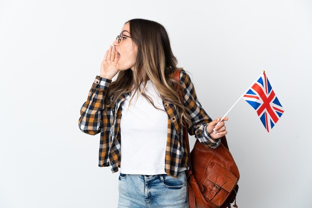 Jeune femme roumaine tenant un drapeau du Royaume-Uni isolé sur un mur blanc en criant avec la bouche grande ouverte sur le côté