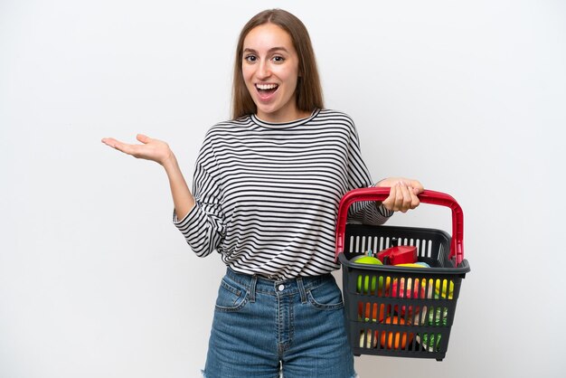 Jeune femme roumaine tenant un panier plein de nourriture isolé sur fond blanc avec une expression faciale choquée