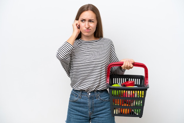 Jeune femme roumaine tenant un panier plein de nourriture isolé sur fond blanc frustré et couvrant les oreilles