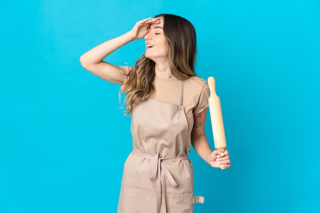 Jeune femme roumaine tenant un rouleau à pâtisserie isolé sur mur bleu souriant beaucoup